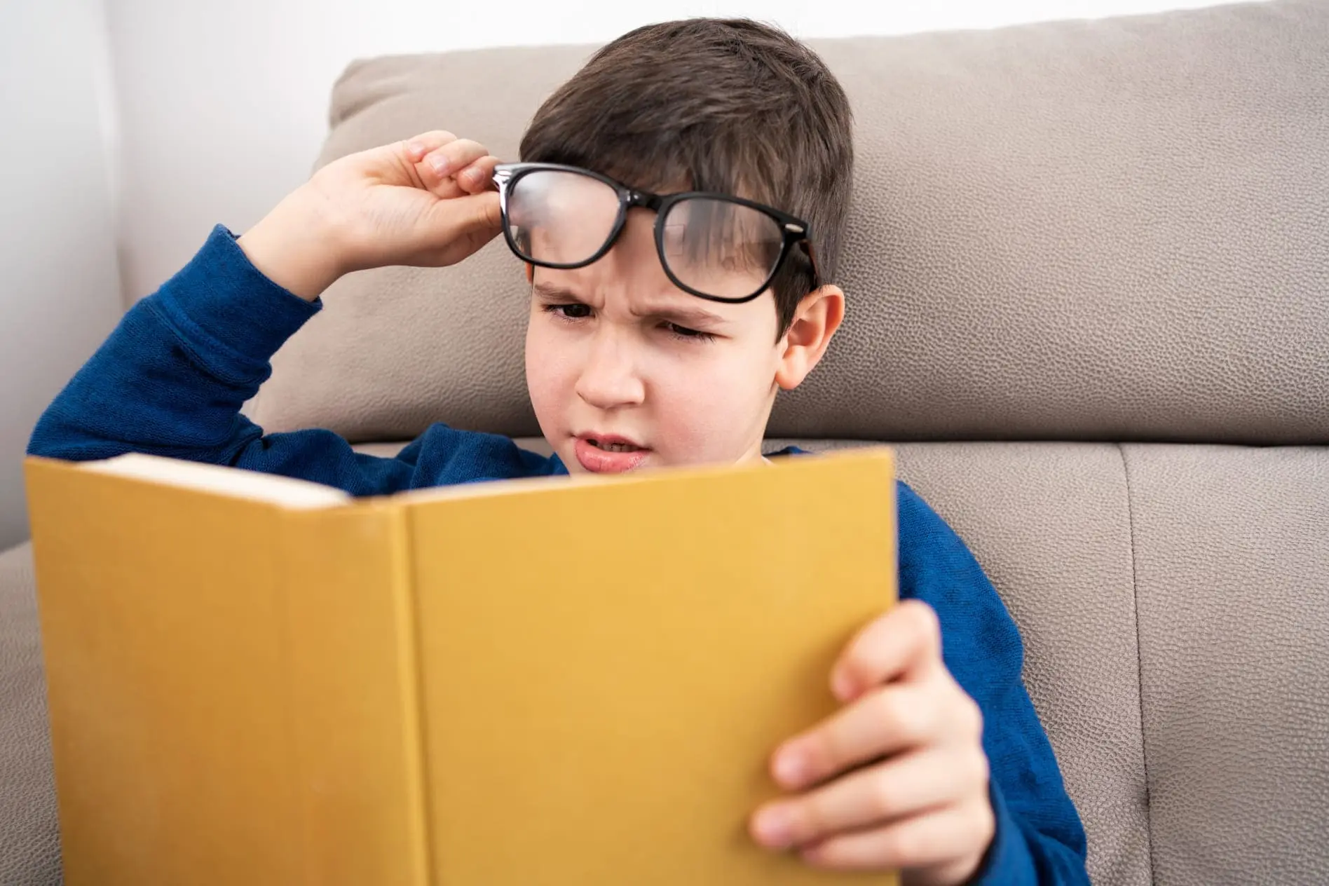 Criança sofre com cansaço visual ao tentar ler um livro em casa.
