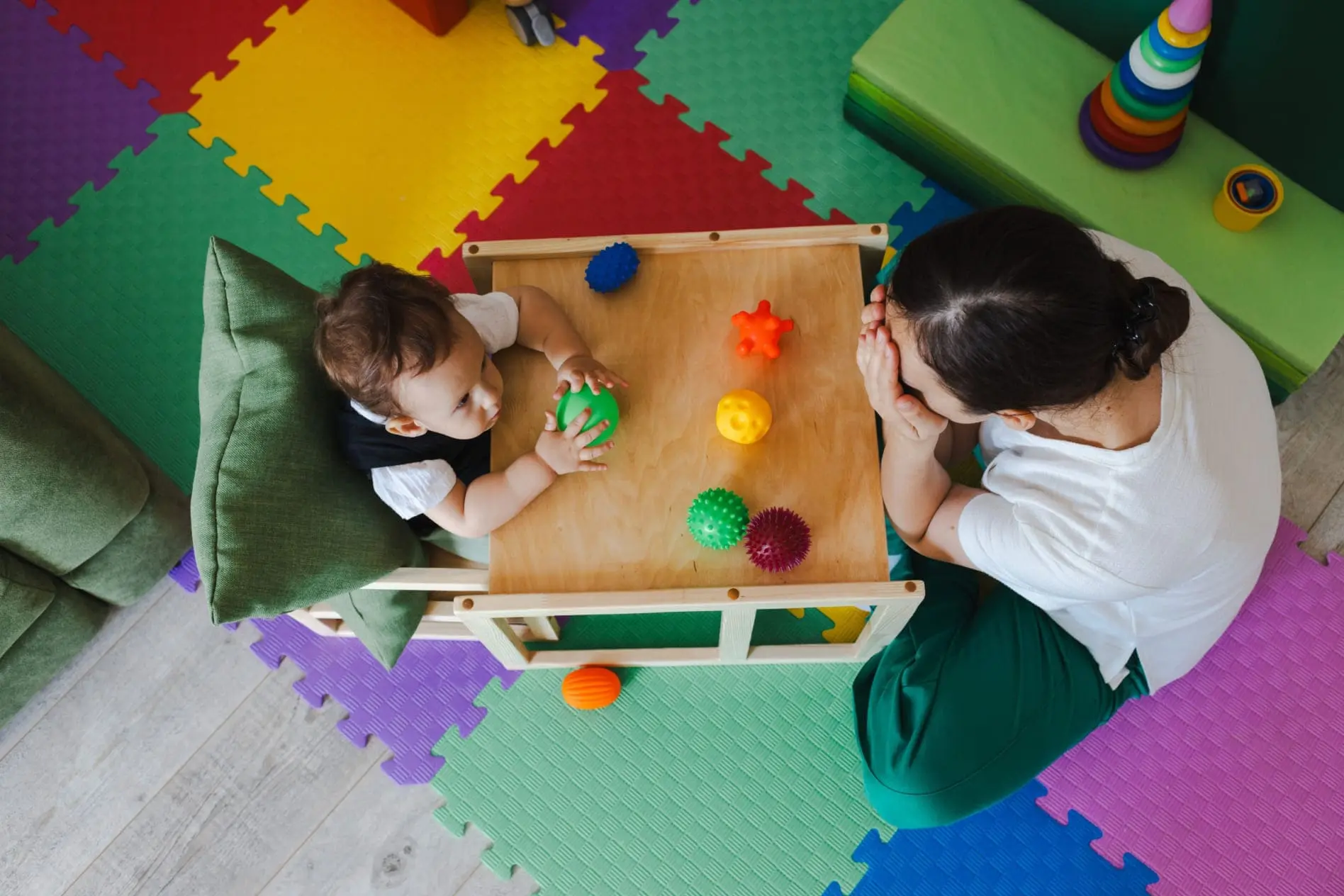 Visão de cima de menino durante terapia ocupacional infantil segurando uma bola colorida para o desenvolvimento de sensibilidades sensoriais.